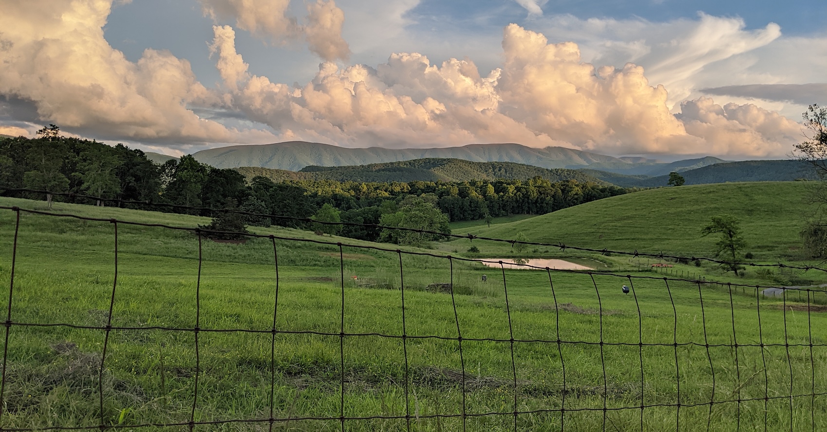 landscape view of green pastures with mountains in the background and puffy clouds in the sky