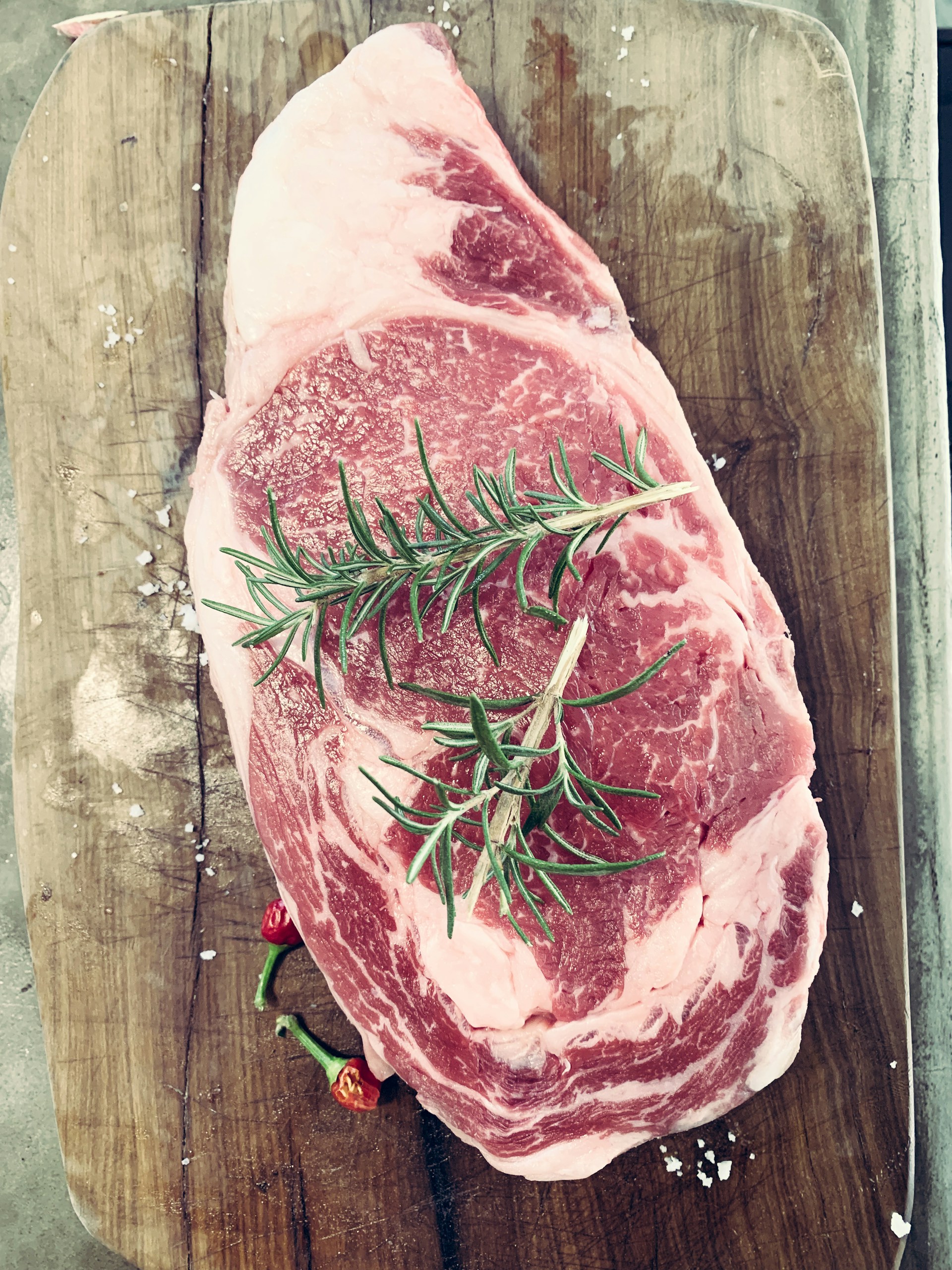 large cut of raw steak on a board with a sprig of rosemary on top