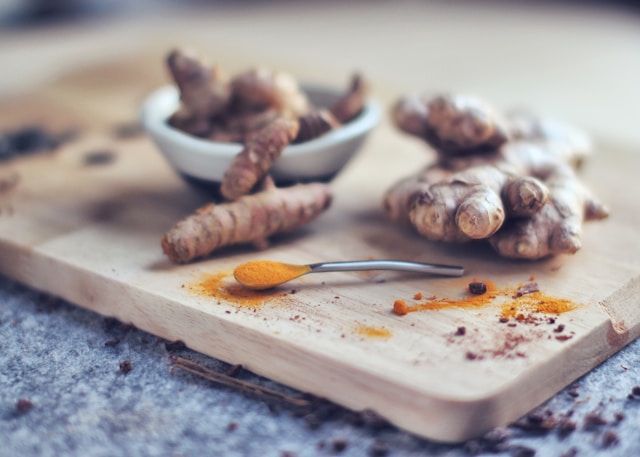 tumeric root on a rustic cutting board with a spoonful of dried tumeric in the foreground